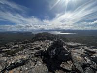 A lake in the background with thin clouds in the sky. Taken from the top of a mountain